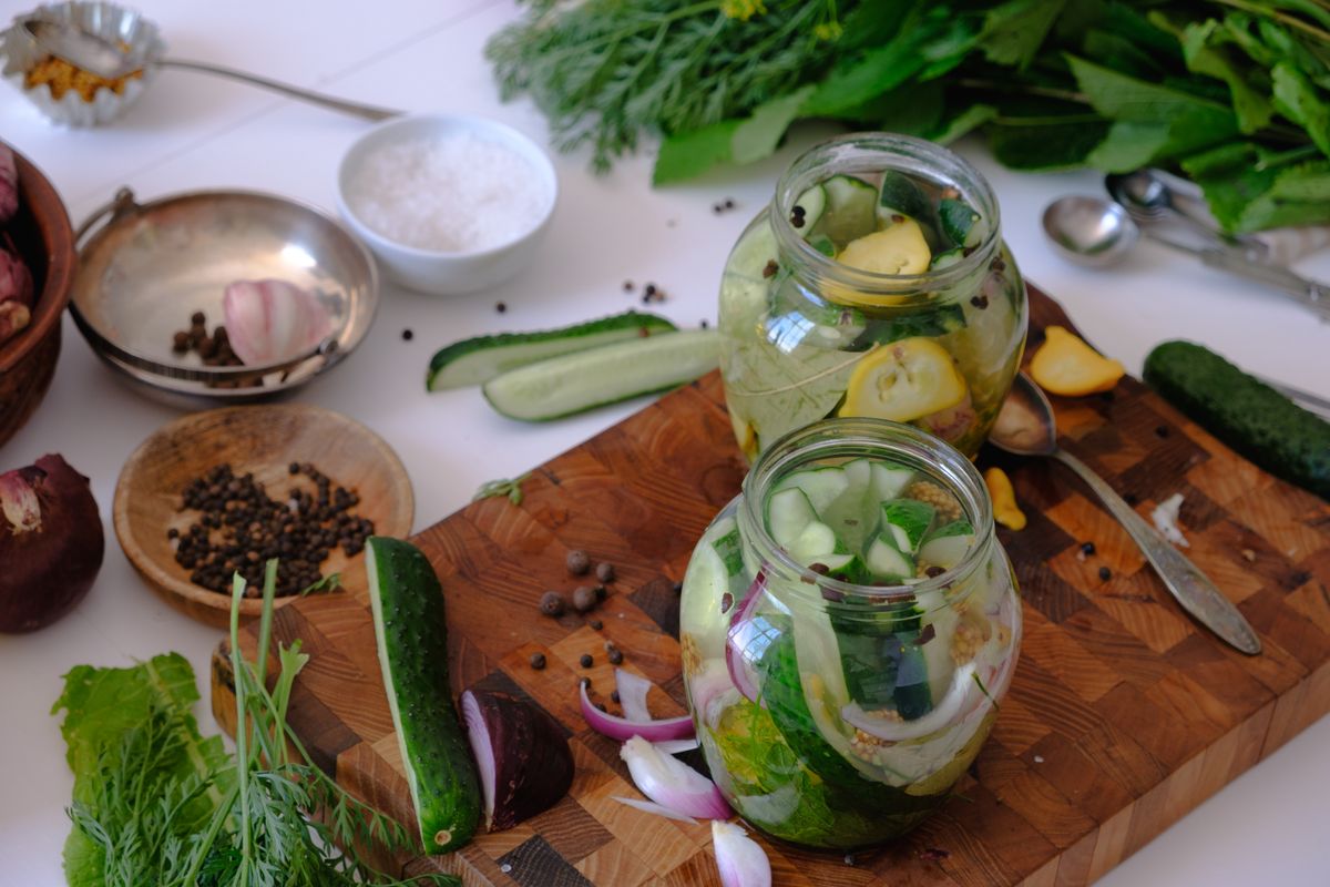 Glass jars of pickles with herbs and spices on a board