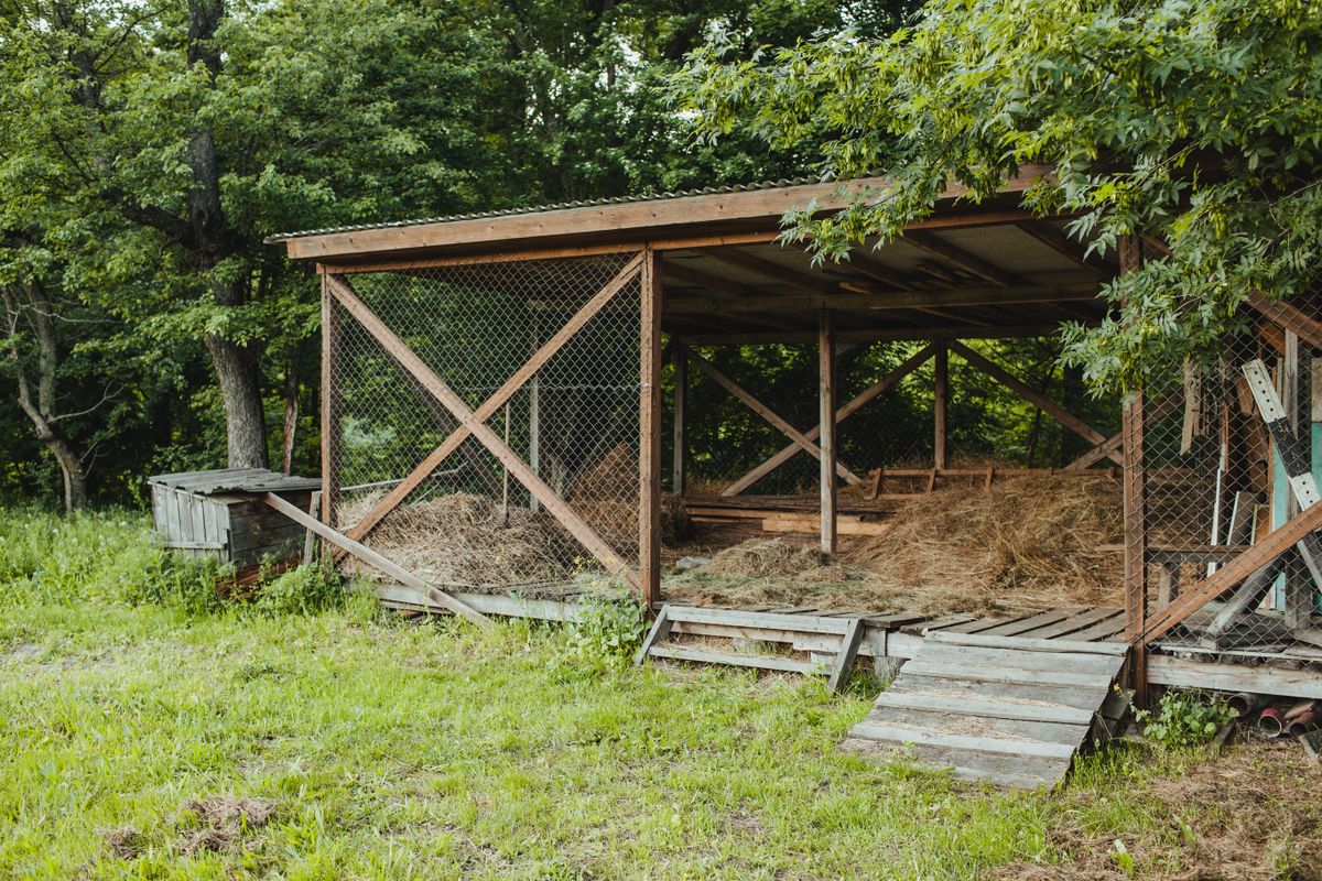 A small wooden coop with straw inside, standing in a garden