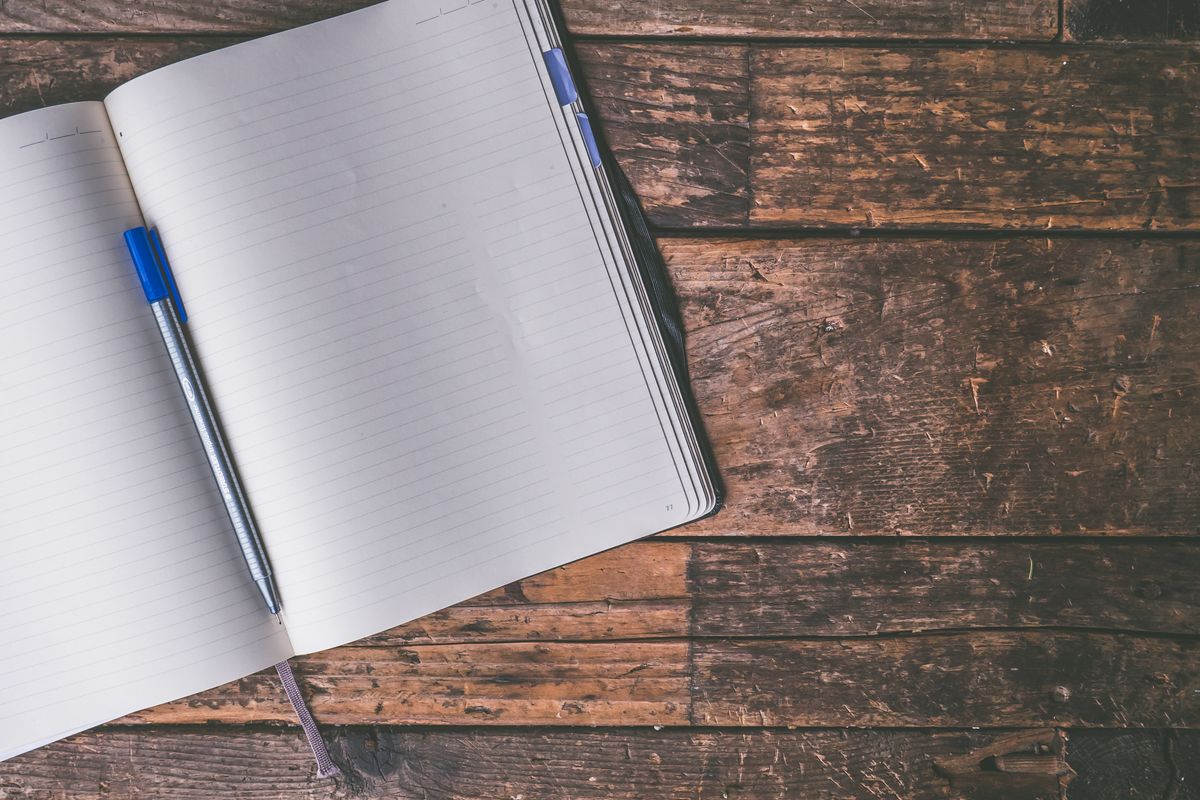 An open notebook and a pen on a wooden table