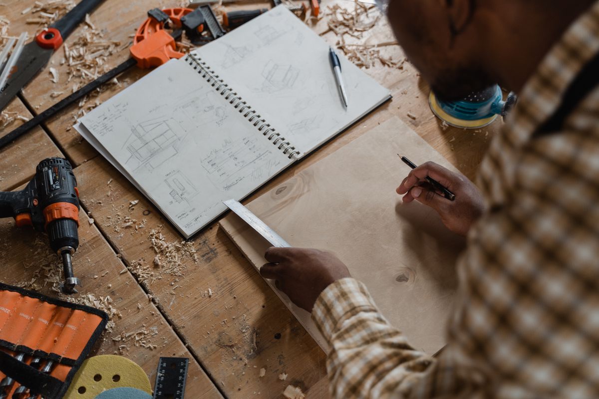 A woodworker sketching plans on a table beside tools