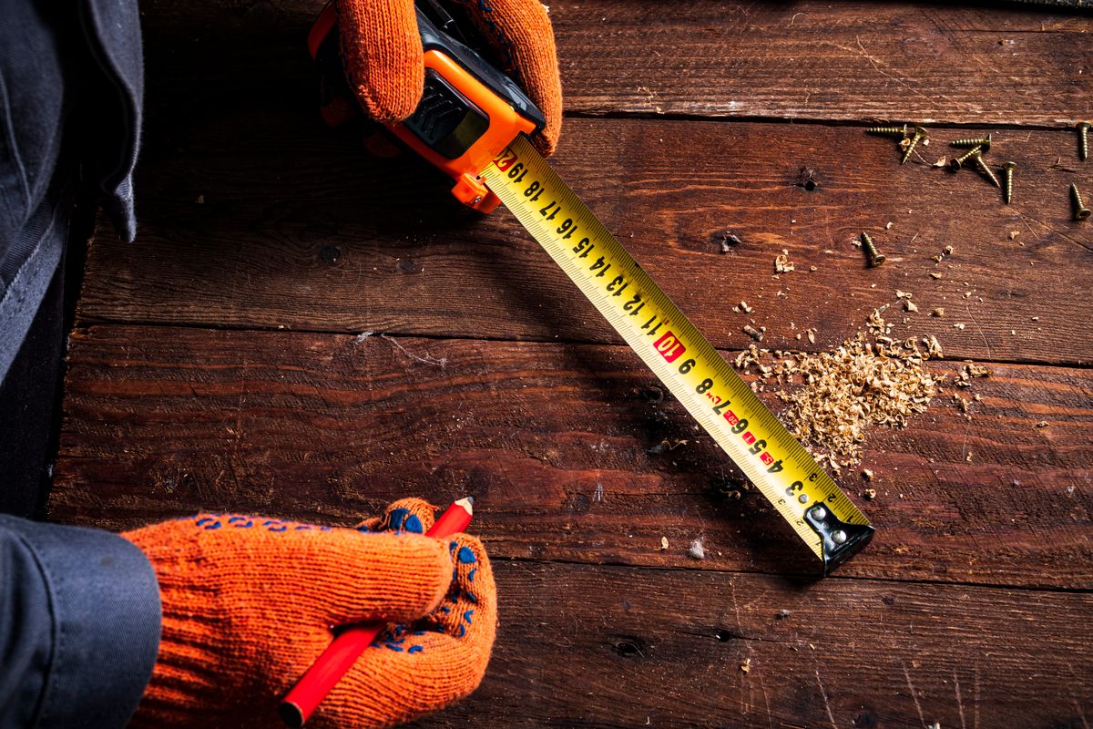 Gloved hands measuring a wooden surface with a tape measure